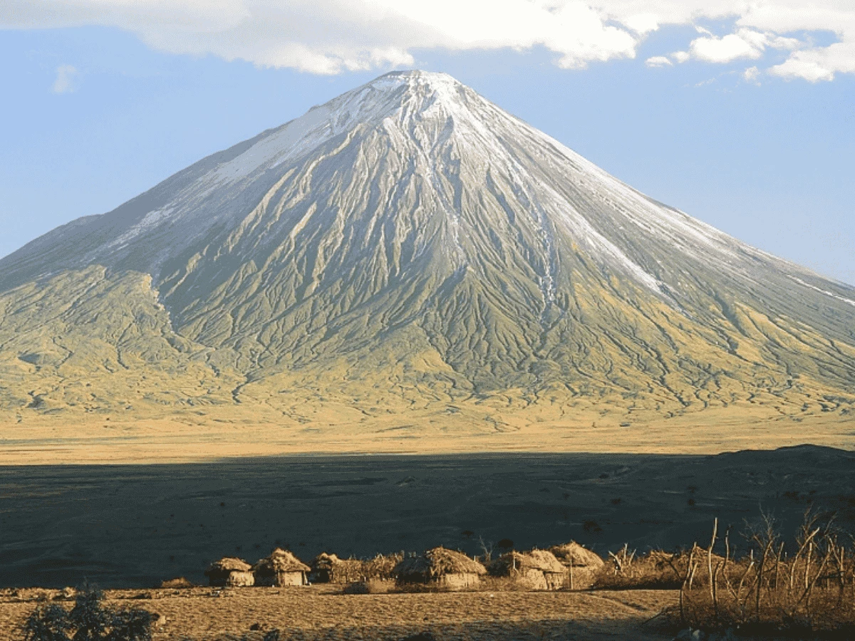 A typical African mud hut village in front of Mount Ol'Doinyo Lengai.